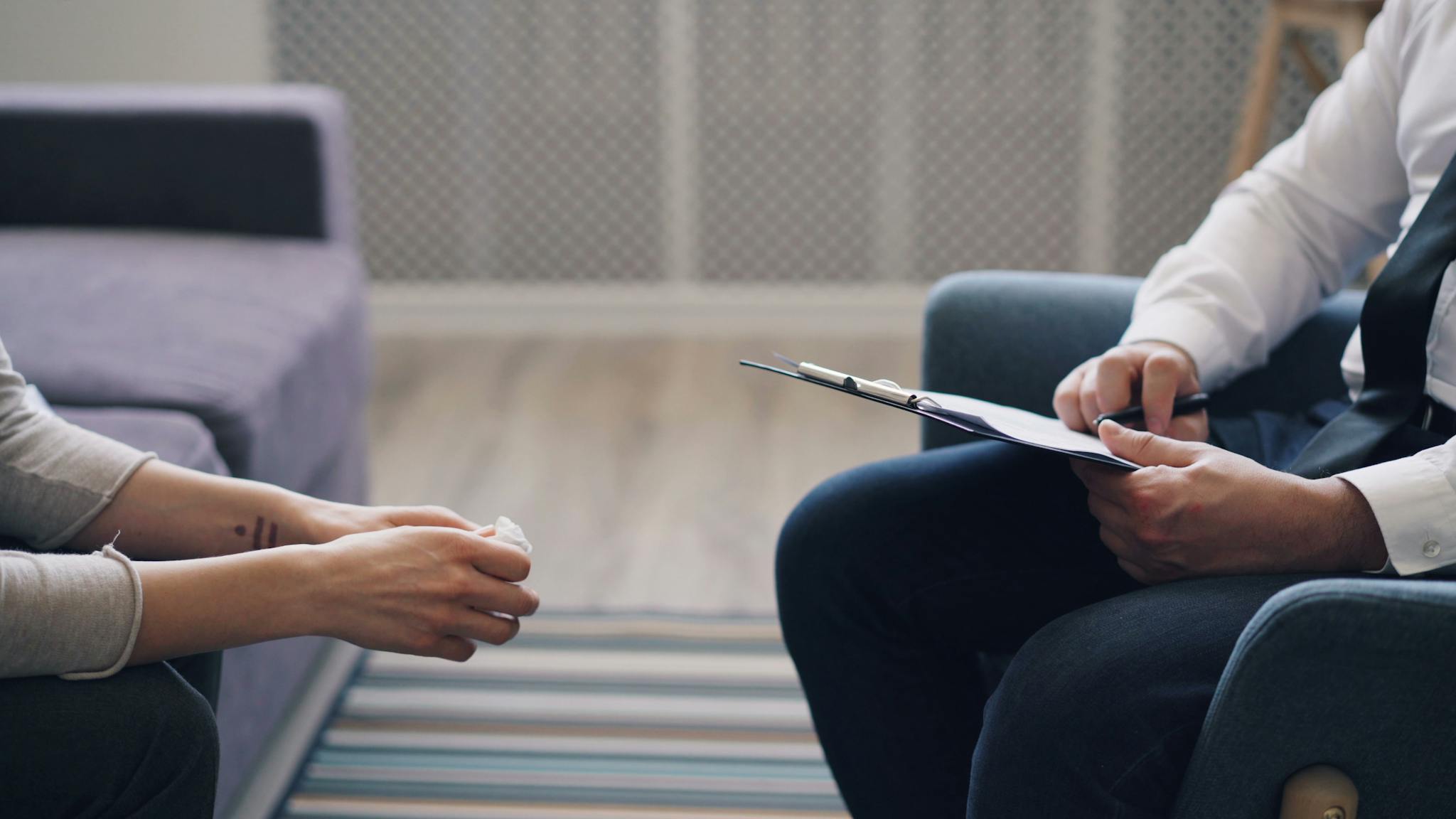 A therapy session with a psychologist and patient, discussing mental health indoors.